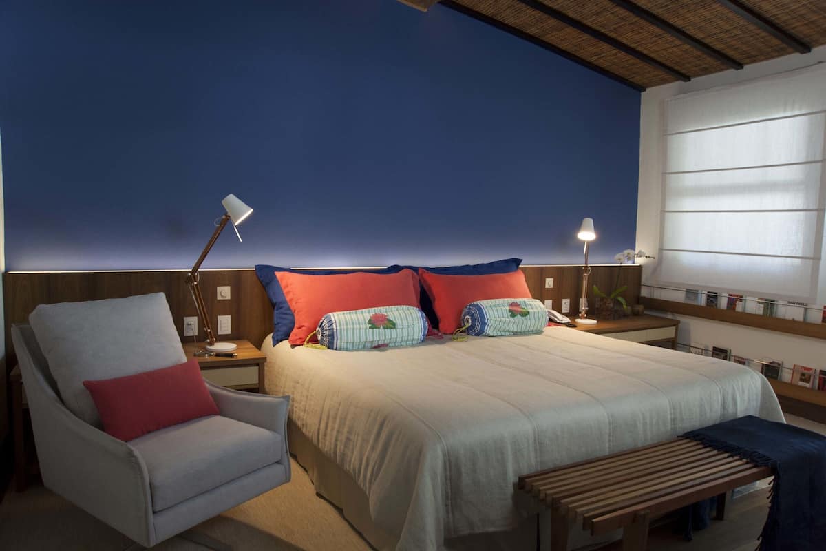 A bedroom with a bed, a chair, bedside tables, lamps, and a window.