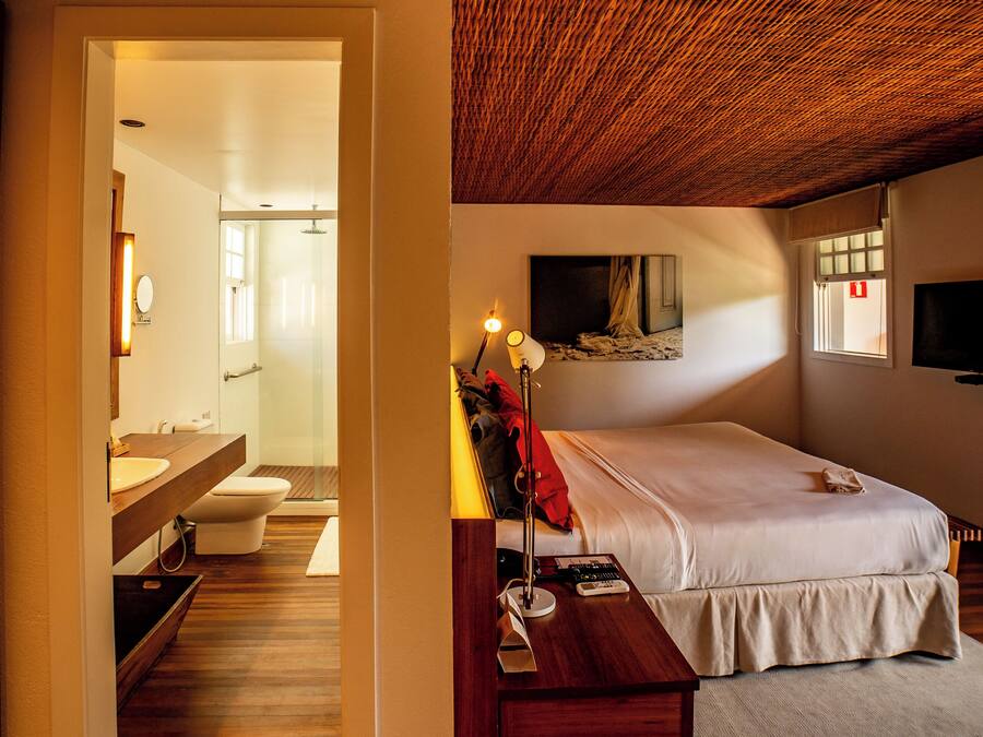 Ein Zimmer mit Holzboden, einem Bett, einem Nachttisch, einer Lampe und einem Gemälde an der Wand.