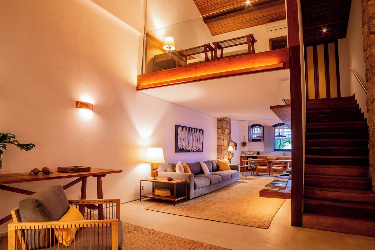 A spacious living area with a high ceiling, a staircase leading to an upper level, and a cozy seating area with a sofa and cushions.