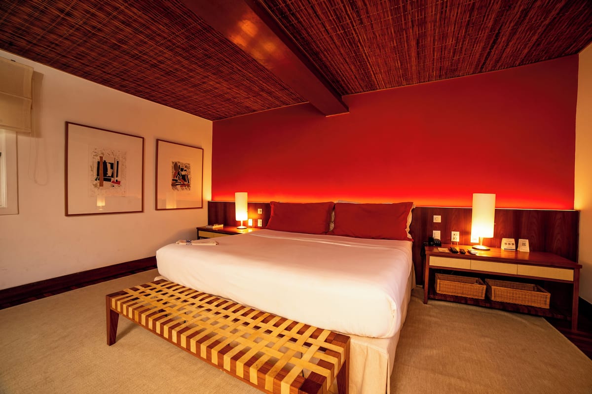 A hotel room with a large bed, wooden headboard, bedside tables, and wall-mounted lamps.