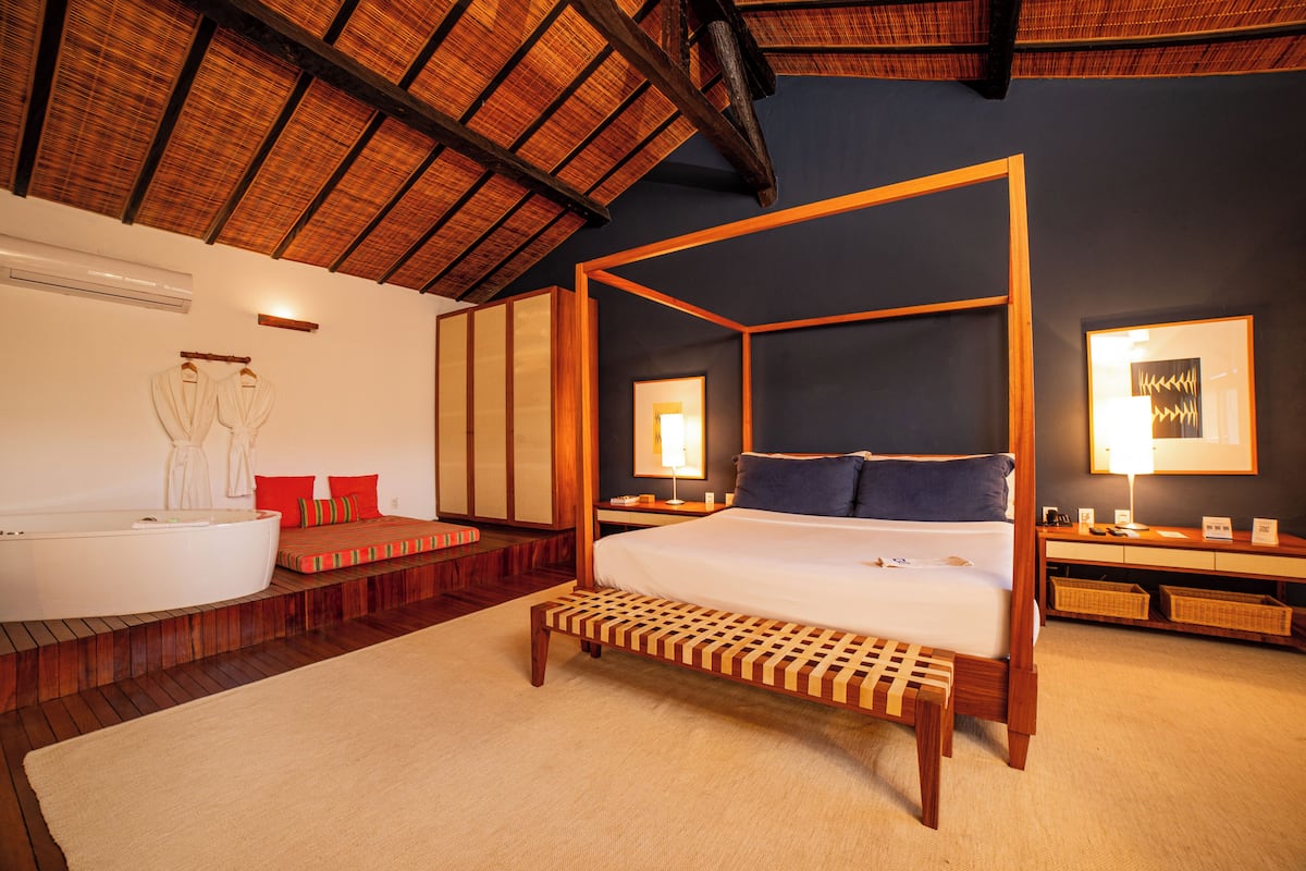 A four-poster bed with a wooden frame, a large bathtub, and a wooden bench.