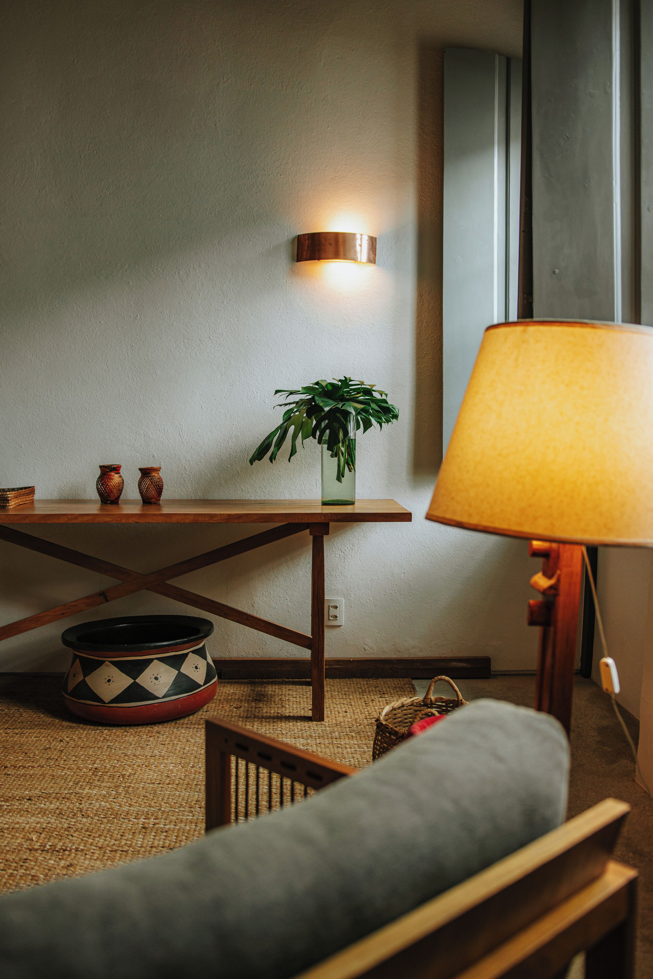 A cozy room with a wooden table, a floor lamp, a grey sofa, and a small potted plant.
