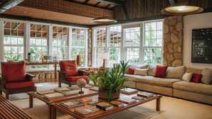 A spacious living room with a large window, a wooden ceiling, and a comfortable sofa. - Pousada Literária (Paraty)