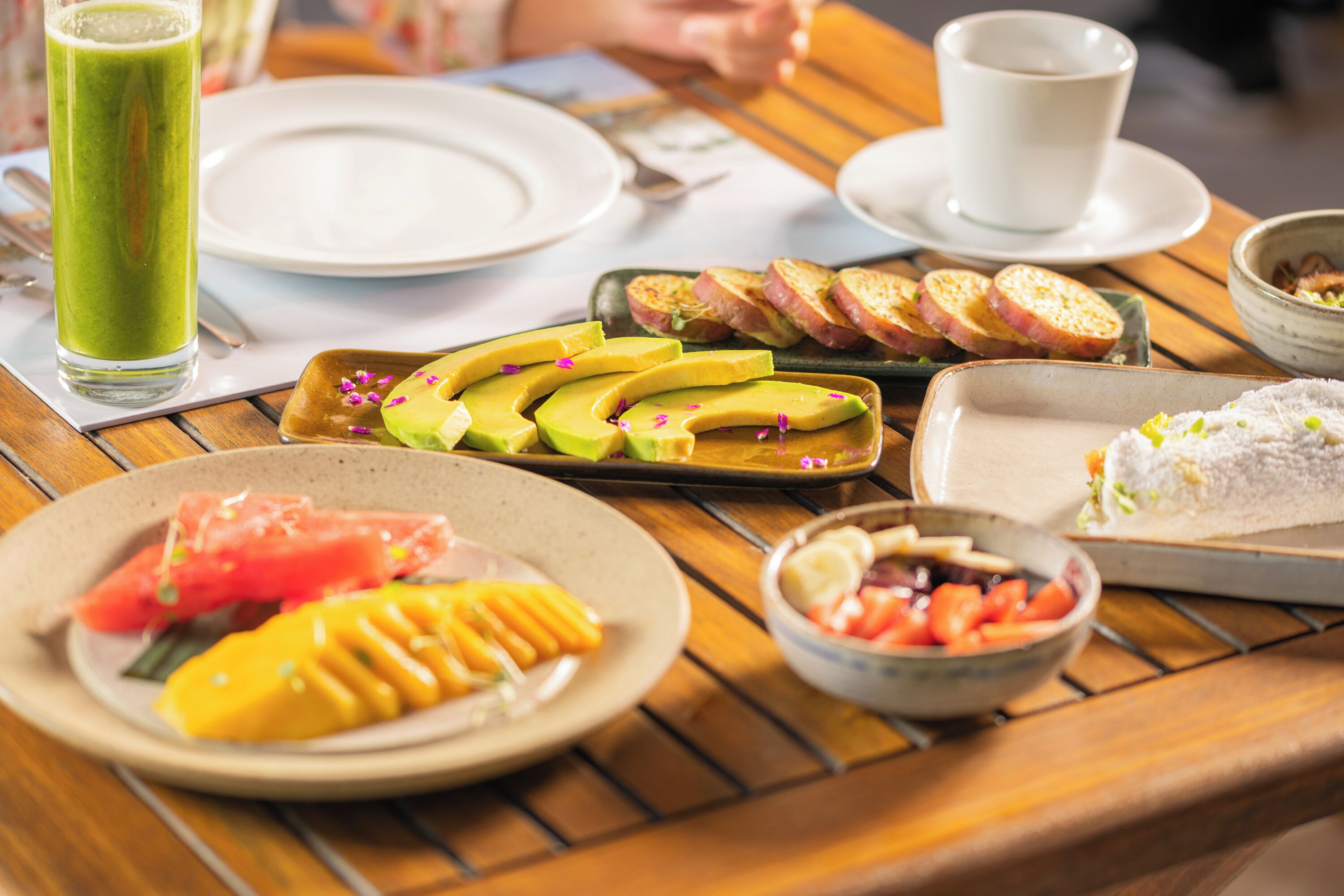 A table with various dishes including sliced avocado, mango, and a bowl of mixed vegetables.