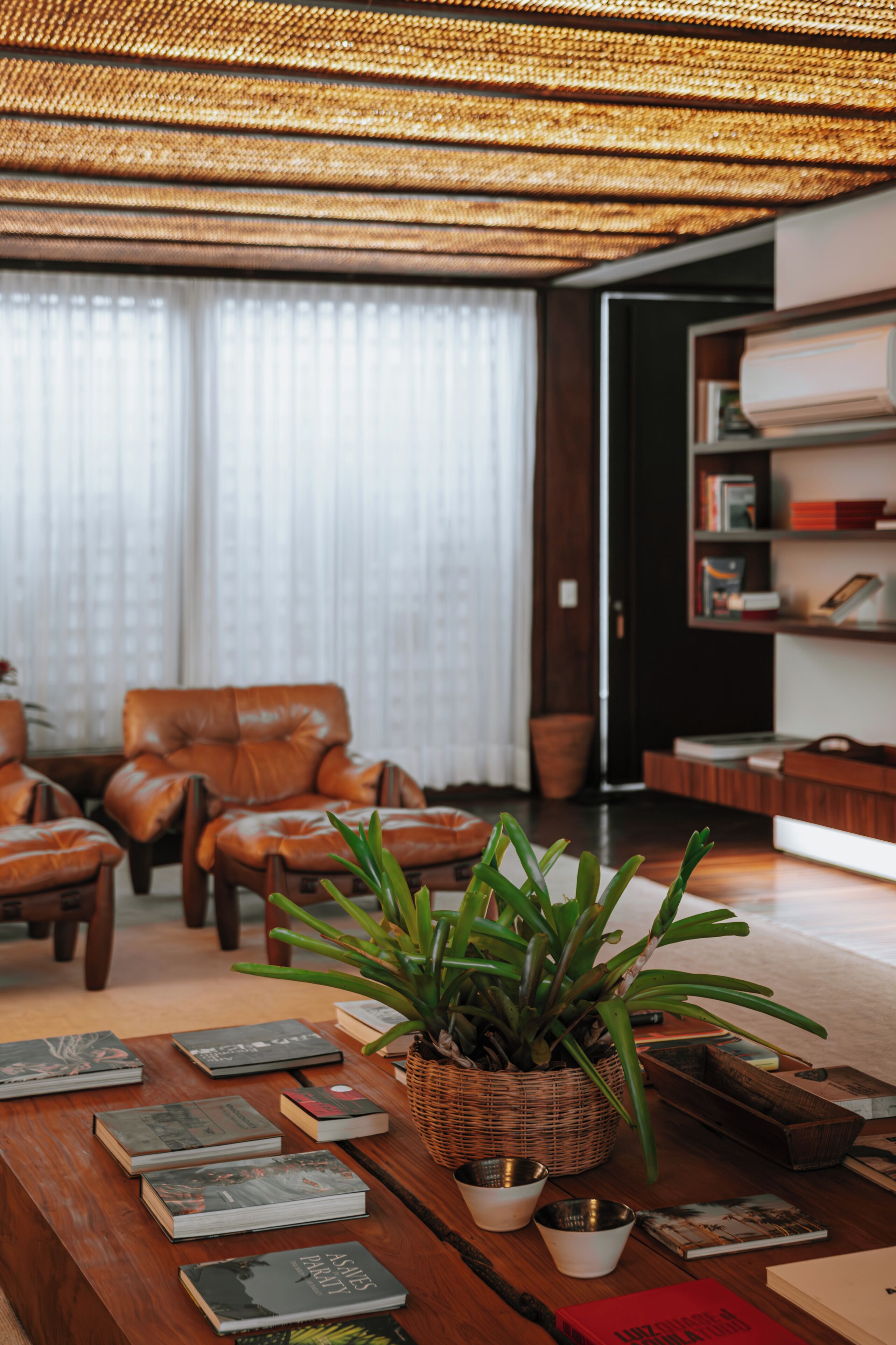 A living room with a wooden coffee table, books, a potted plant, leather chairs, and a bookshelf.