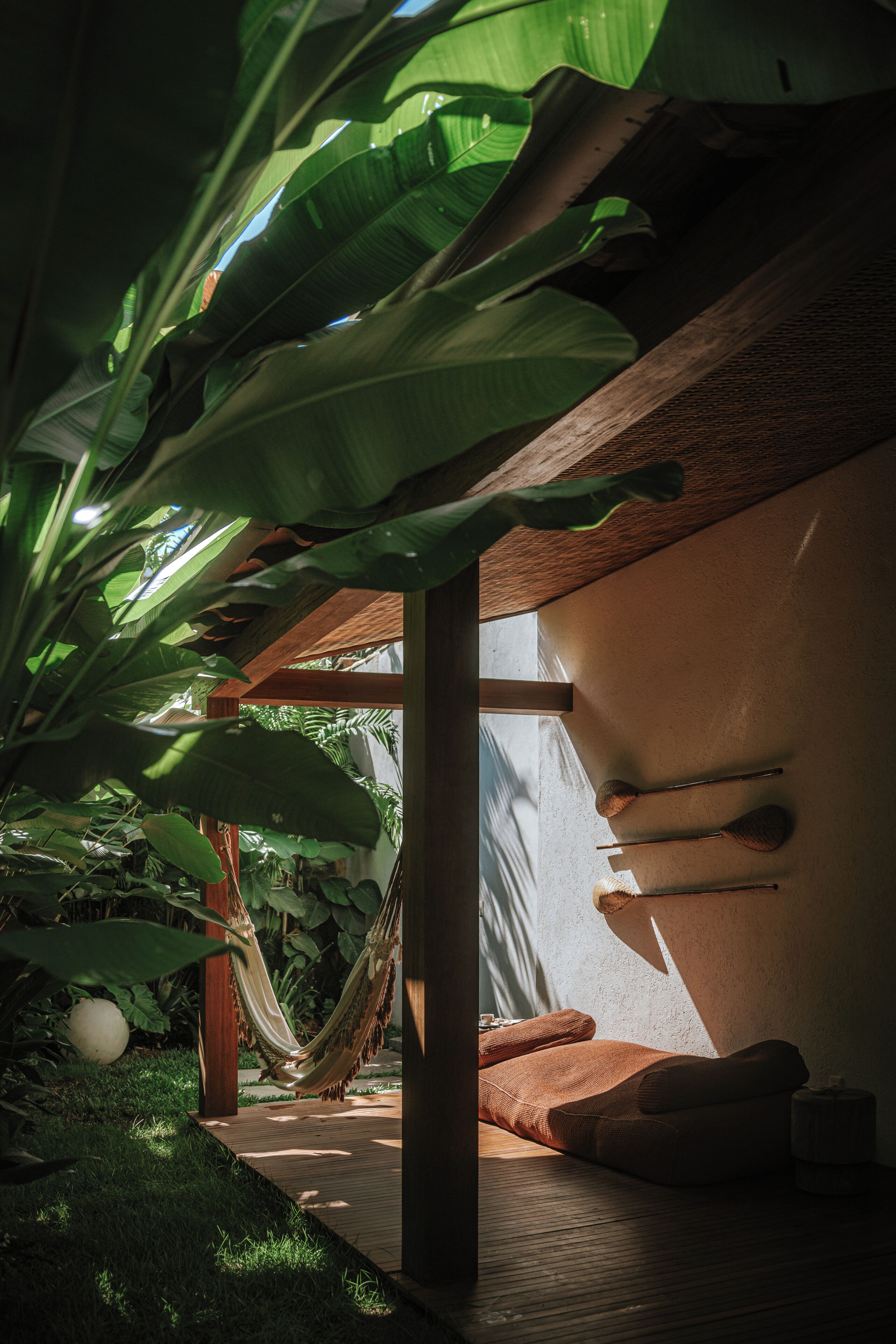 A hammock under large banana leaves, a wooden deck, and a bed with pillows.