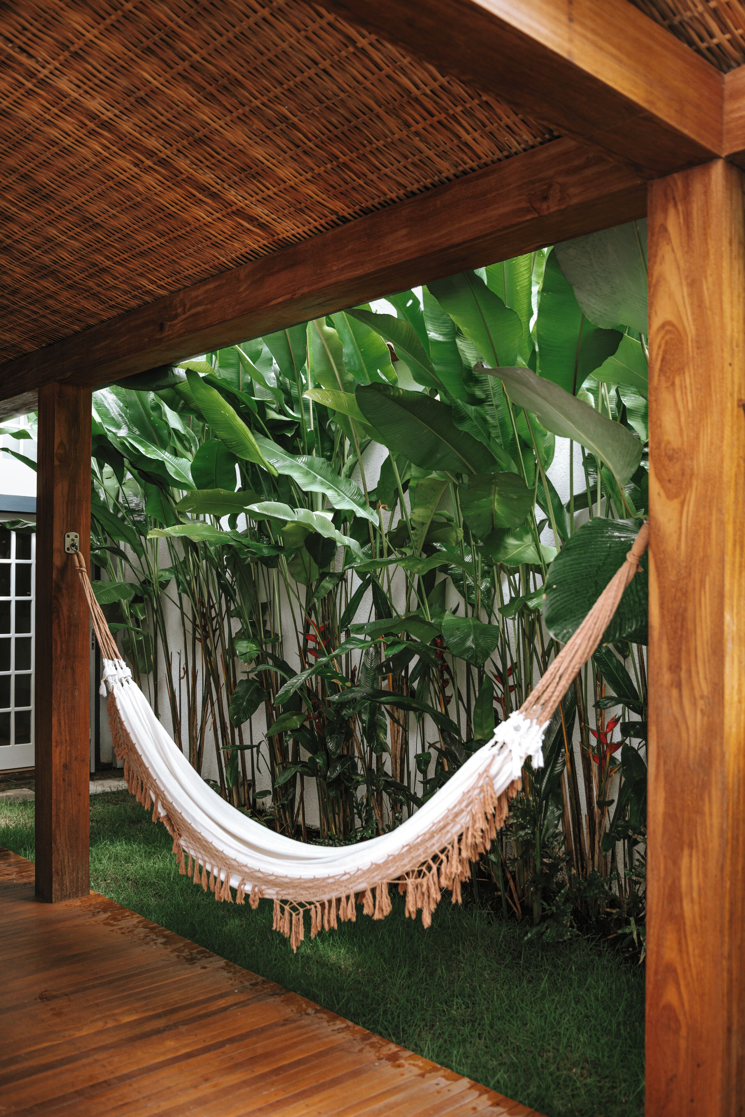 A hammock under a wooden pergola with lush green foliage in the background.