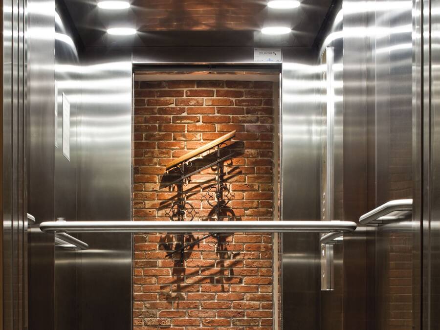 Elevatorinteriør med murstensvæg og ståldøre.