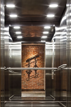 Interior de elevador com parede de tijolos e portas de metal.