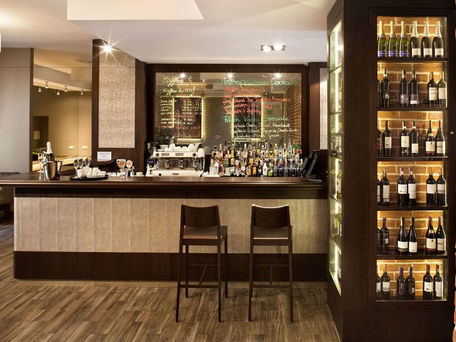 A bar area with a wooden counter, two stools, a wine display, and a menu board.
