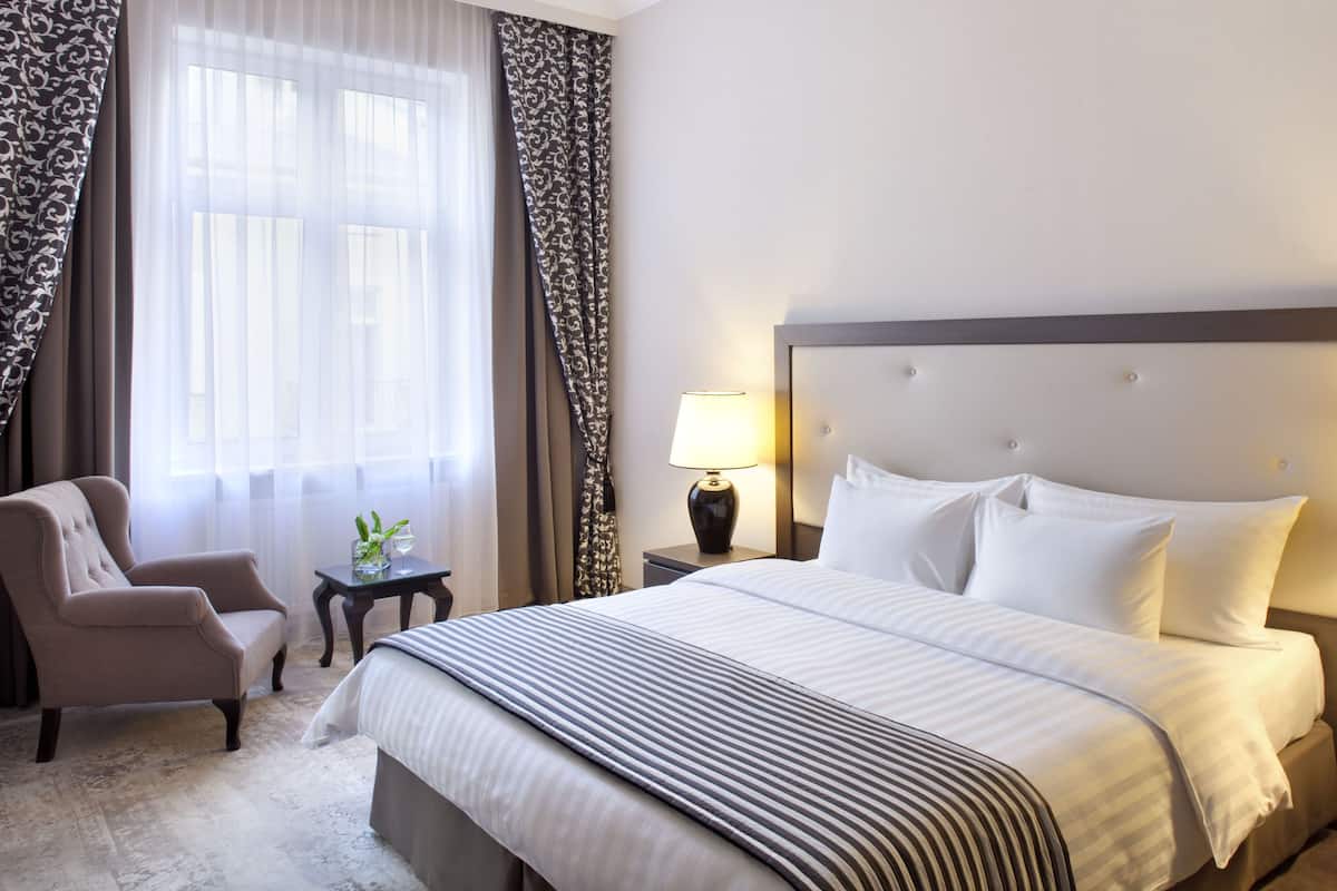 Ein Hotelzimmer mit einem großen Bett, einem Sessel, einem Nachttisch mit Lampe und einem Fenster mit Vorhängen.