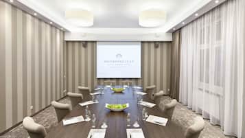 Un salón de conferencias con una larga mesa, sillas, una pantalla de proyector mostrando 'Metropolitan Boutique Hotel' y un frutero sobre la mesa.