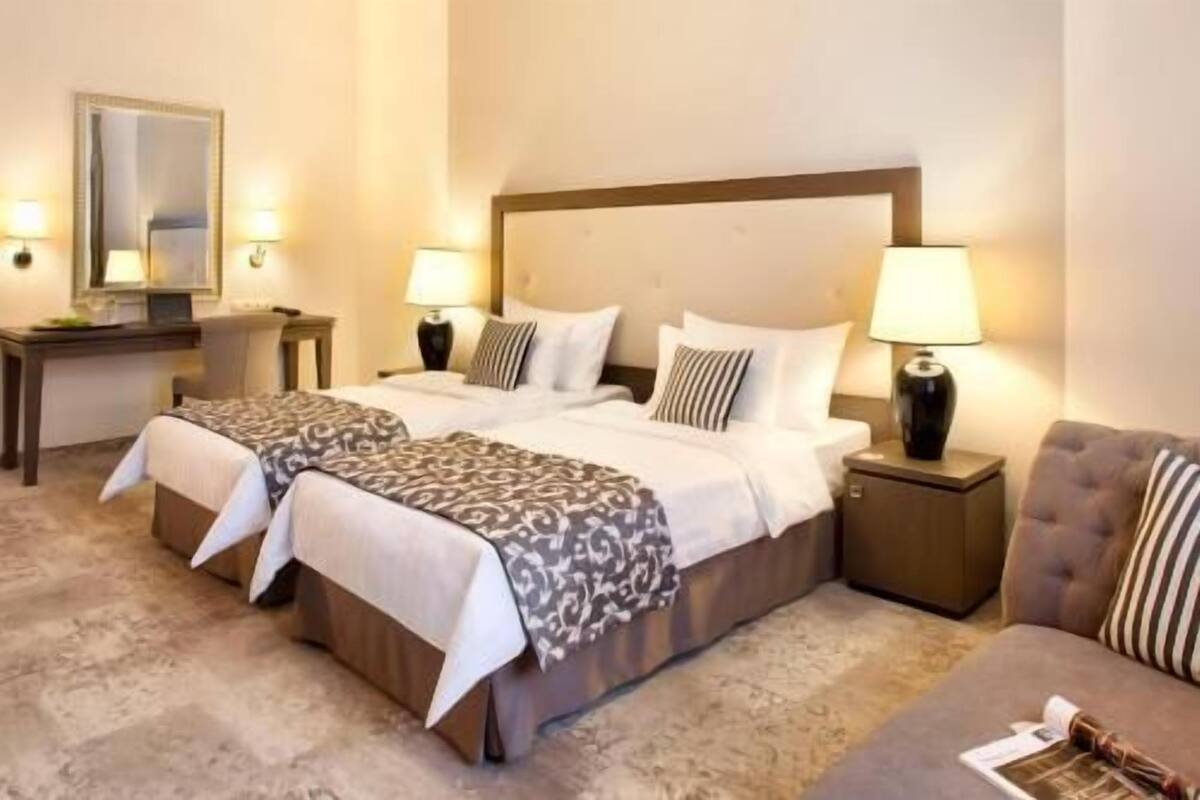 Ein Hotelzimmer mit zwei Betten, einem Nachttisch mit Lampe, einem kleinen Tisch und einem Sofa.