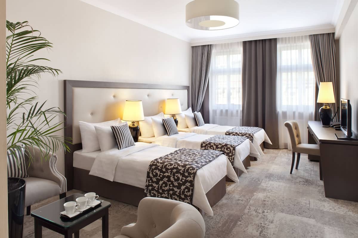 Ein Hotelzimmer mit zwei Betten, einem Schreibtisch, einem Sessel, einem Couchtisch und einer Zimmerpflanze.