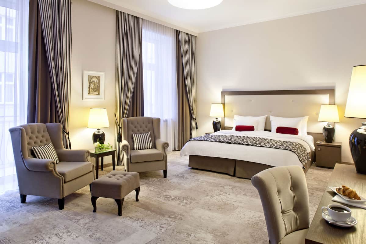 Ein Hotelzimmer mit einem großen Bett, zwei Sesseln, einem kleinen Tisch mit einer Lampe und einem Couchtisch.