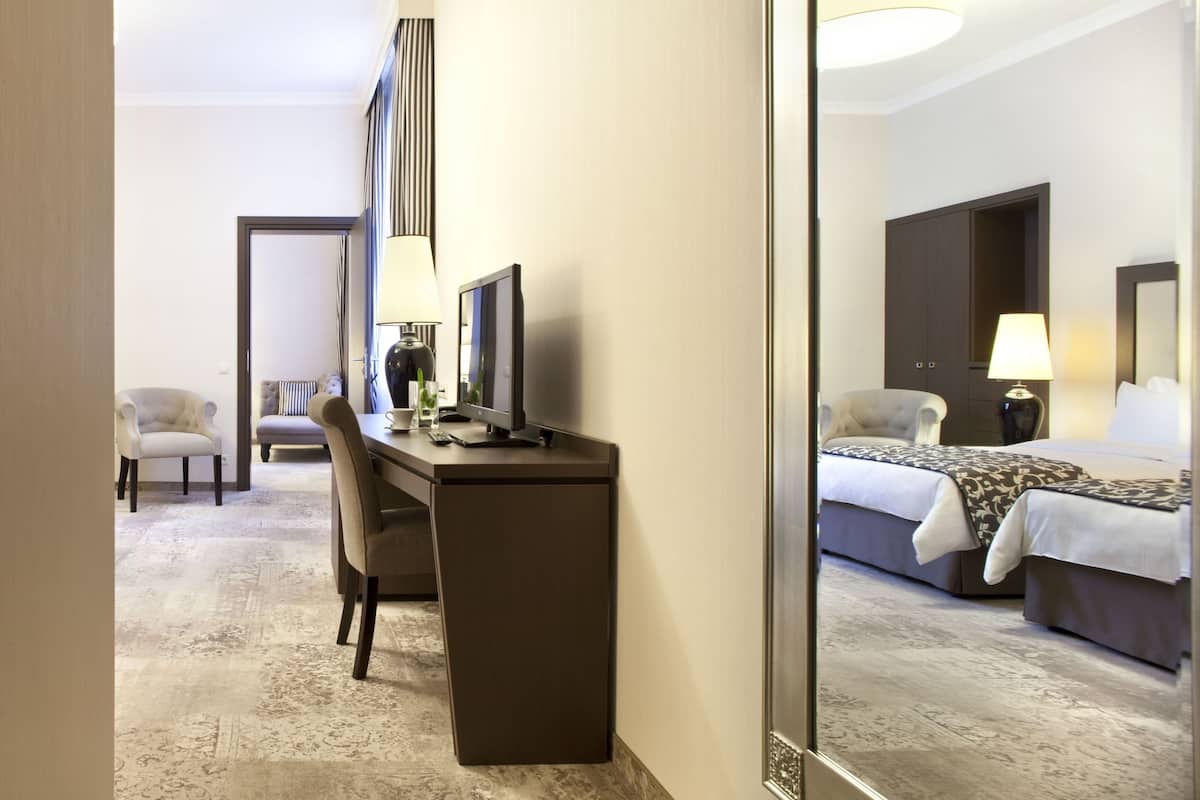 Ein Hotelzimmer mit Schreibtisch, Stuhl, Bett, Nachttisch, Lampe und einem großen Spiegel.