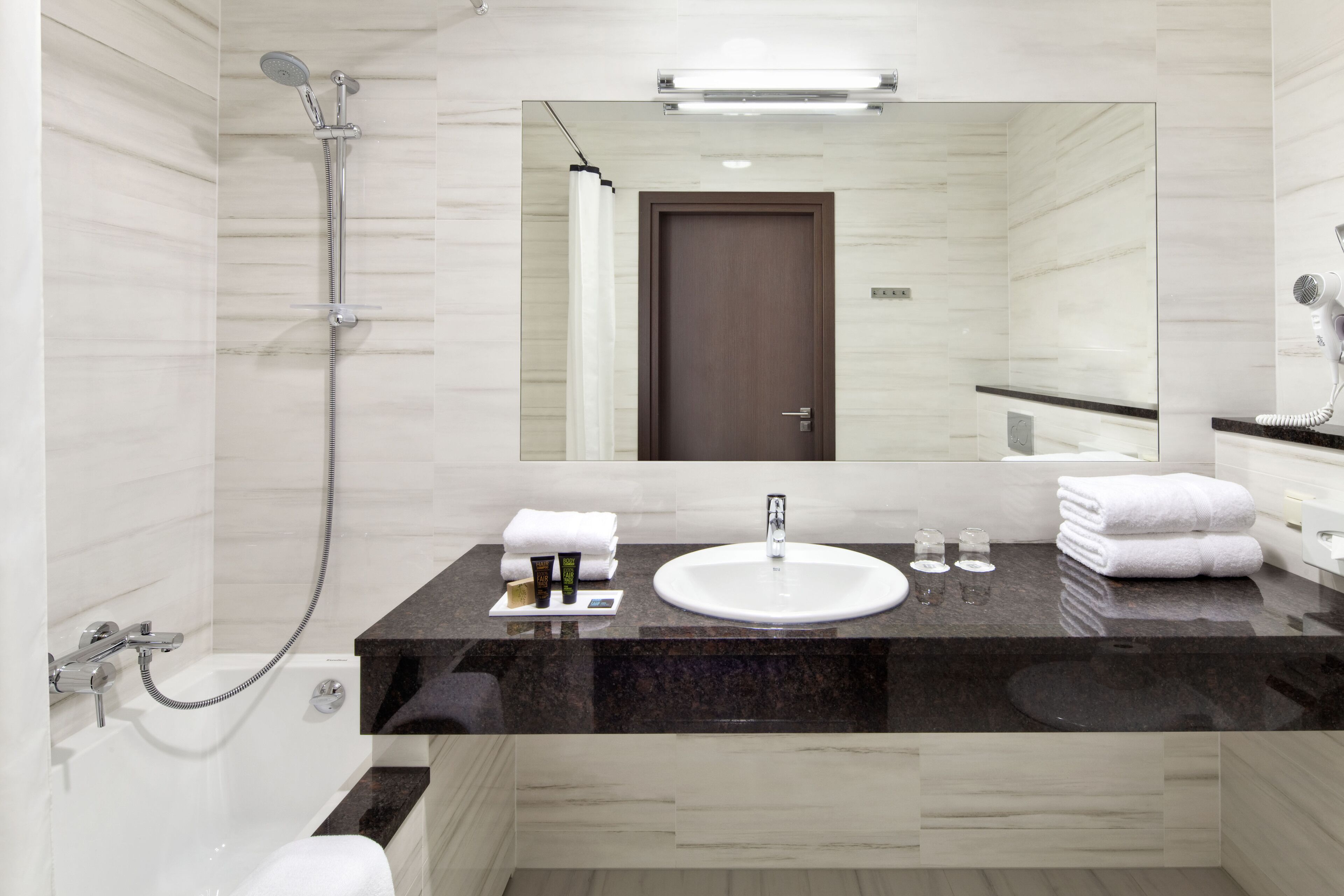 A modern bathroom with a marble vanity, a large mirror, a shower, and a hairdryer on the counter.