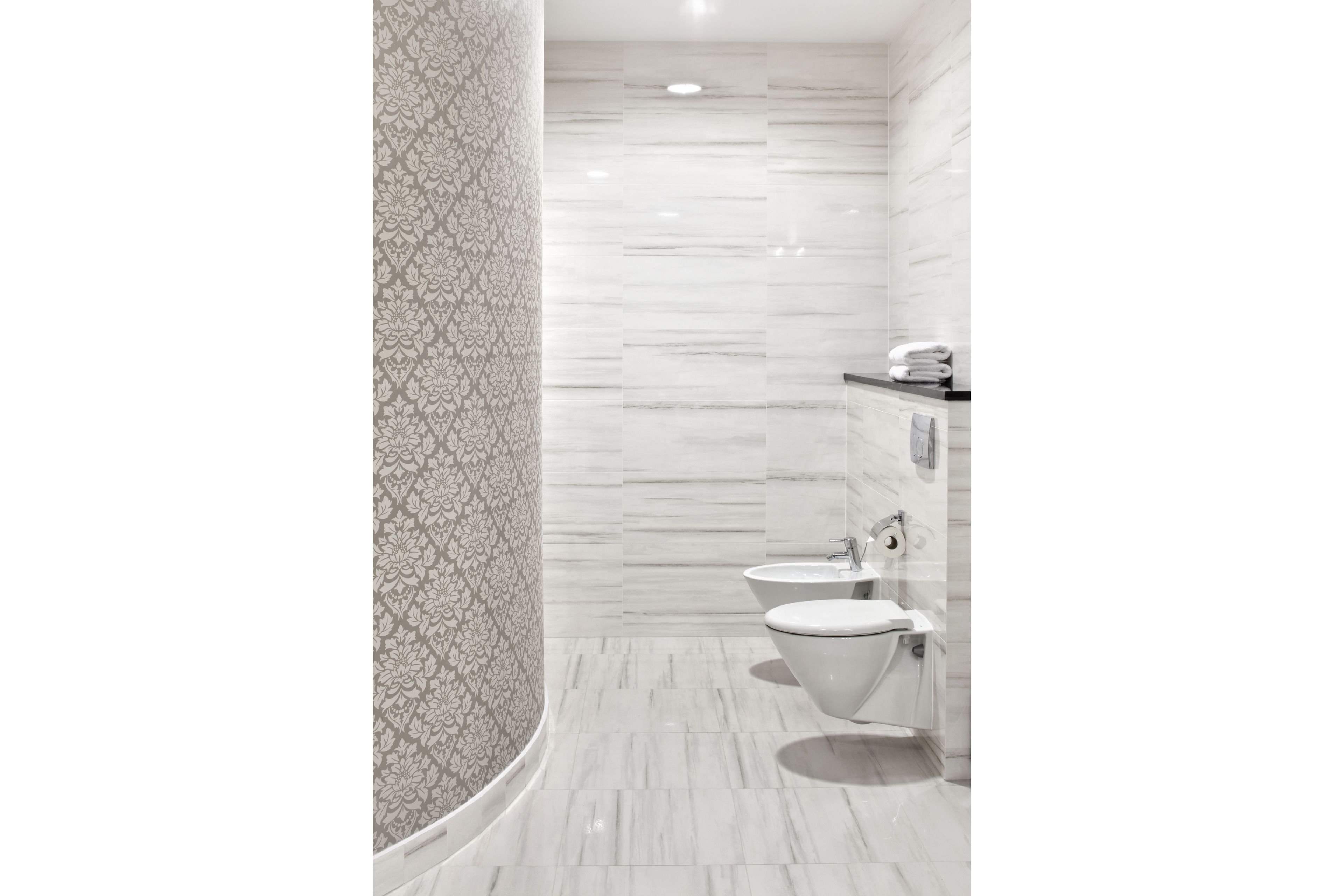 A modern bathroom with a patterned wall, a toilet, and a shower area.