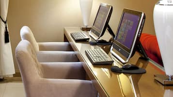 A hotel room with a wooden desk, two laptops, a keyboard, a mouse, and two chairs.