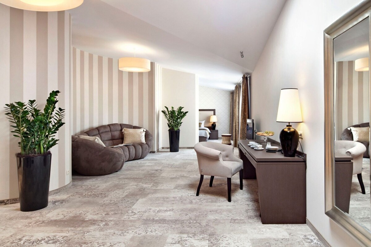 Vestíbulo de hotel con sofá, sillón, escritorio y plantas en macetas.