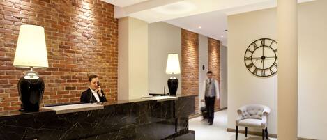 A reception area with a marble counter, two lamps, a clock, and a white chair.