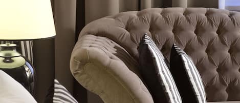 Un sillón con textura, almohadas a rayas, una lámpara de noche y vistas a cortinas y una ventana.