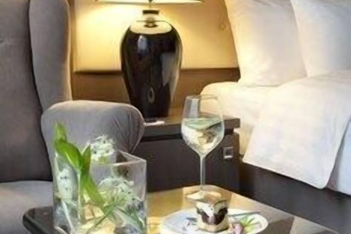 Ein Hotelzimmer mit einem Bett, einem Sofa, einem Nachttisch mit Lampe sowie einem Tisch mit einem Glas Wasser und einem Dessert.