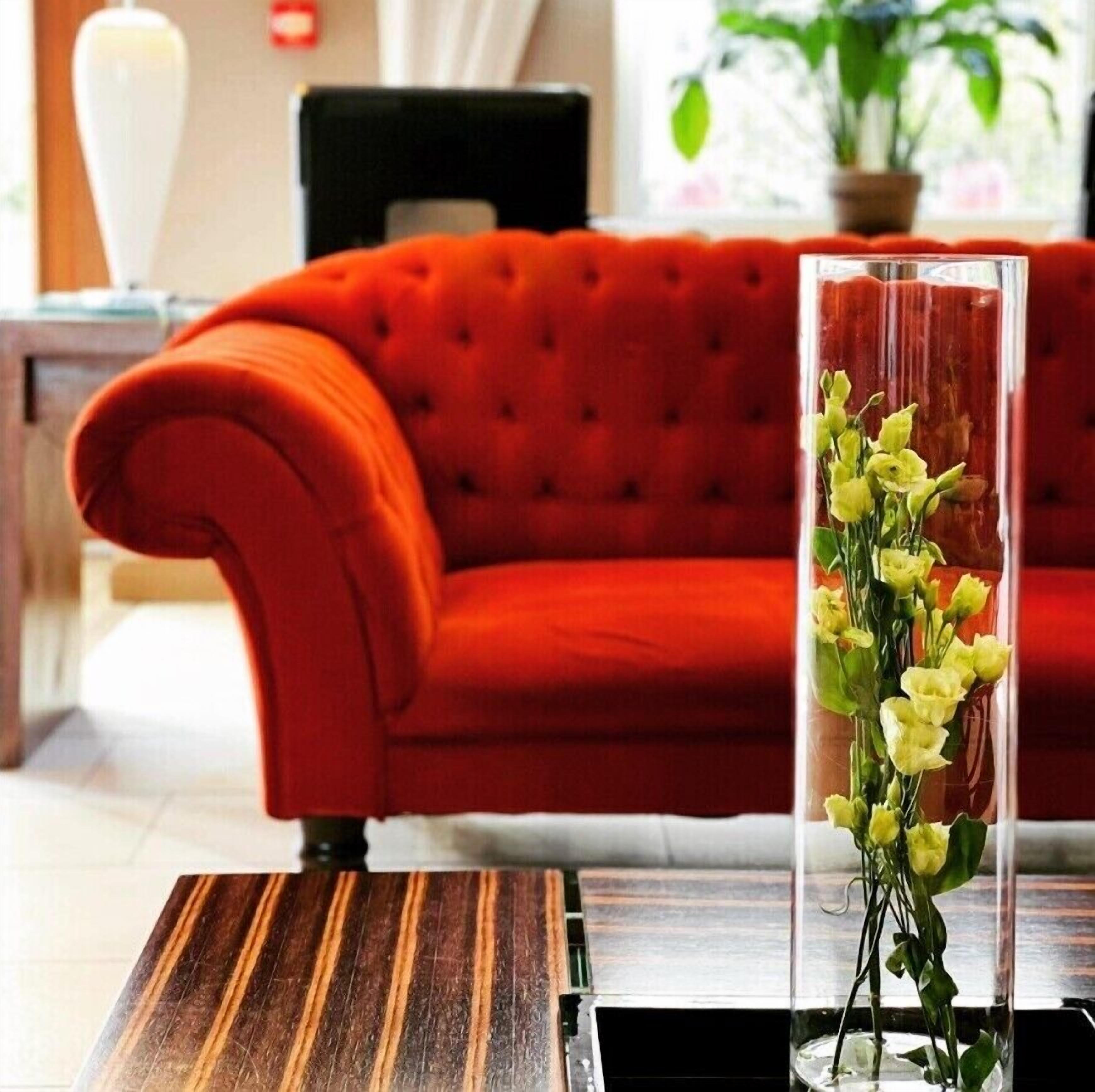 Ein rotes Sofa in einem Zimmer mit einem Holztisch und einer klaren Vase mit gelben Blumen.