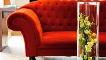 Un canapé rouge dans une pièce où se trouvent une table basse en bois et un vase transparent contenant des fleurs jaunes.