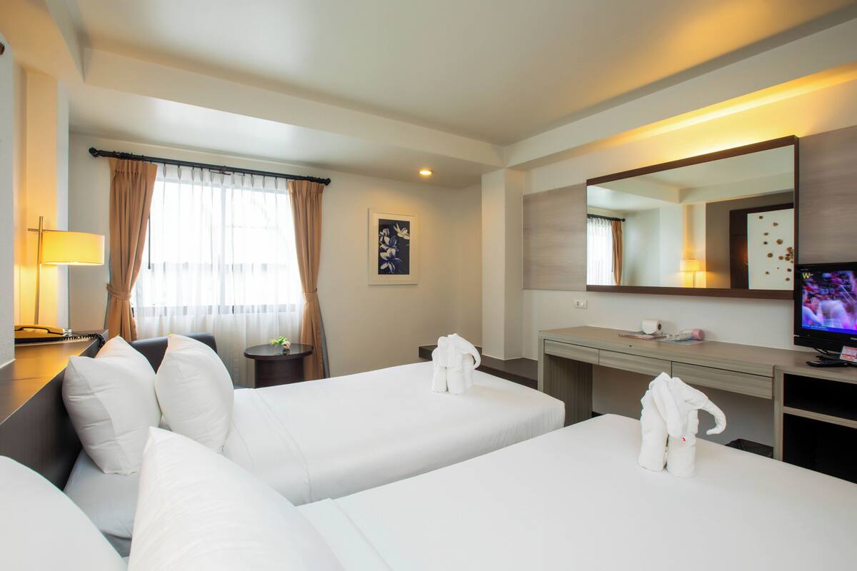 A hotel room with two beds, a desk, a television, and a window with curtains.