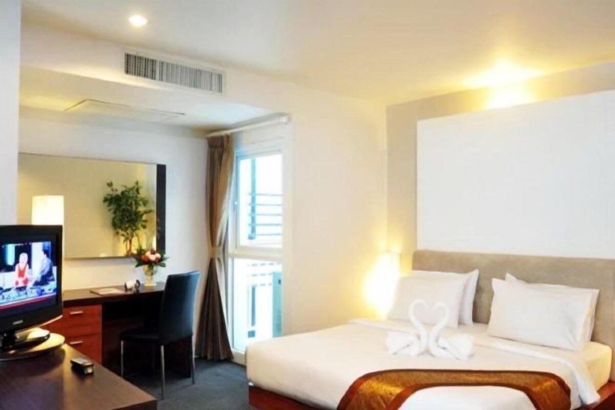 A hotel room with a bed, a desk with a television, a chair, and a window with curtains.