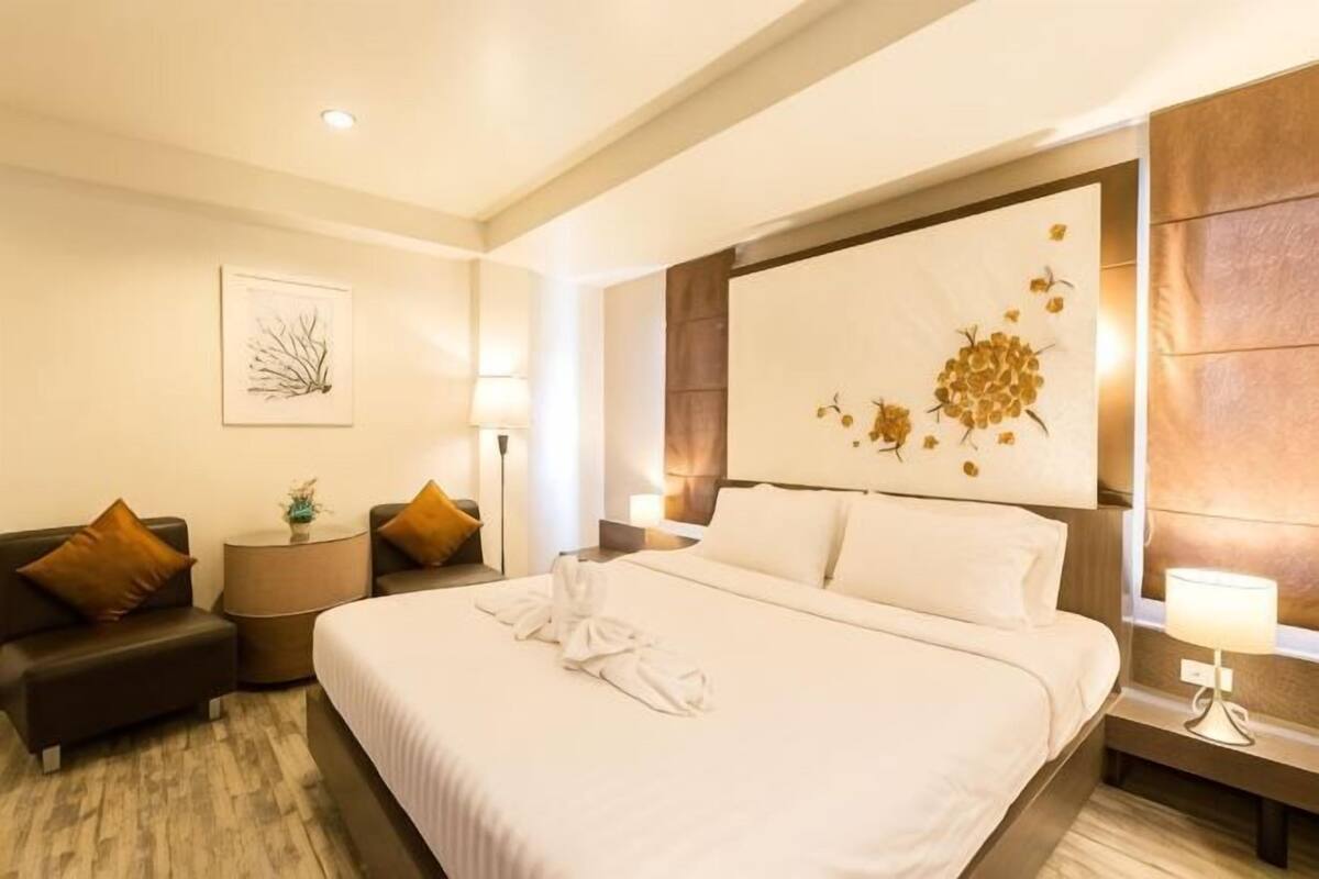 A hotel room with a large bed, a sofa, a bedside table, and a wall-mounted artwork.