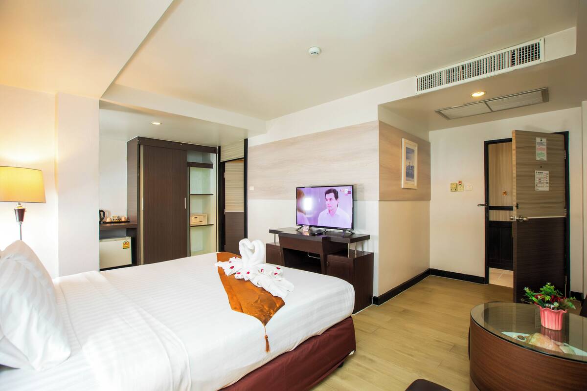 A hotel room with a bed, a TV, a desk, and a small table with a plant.