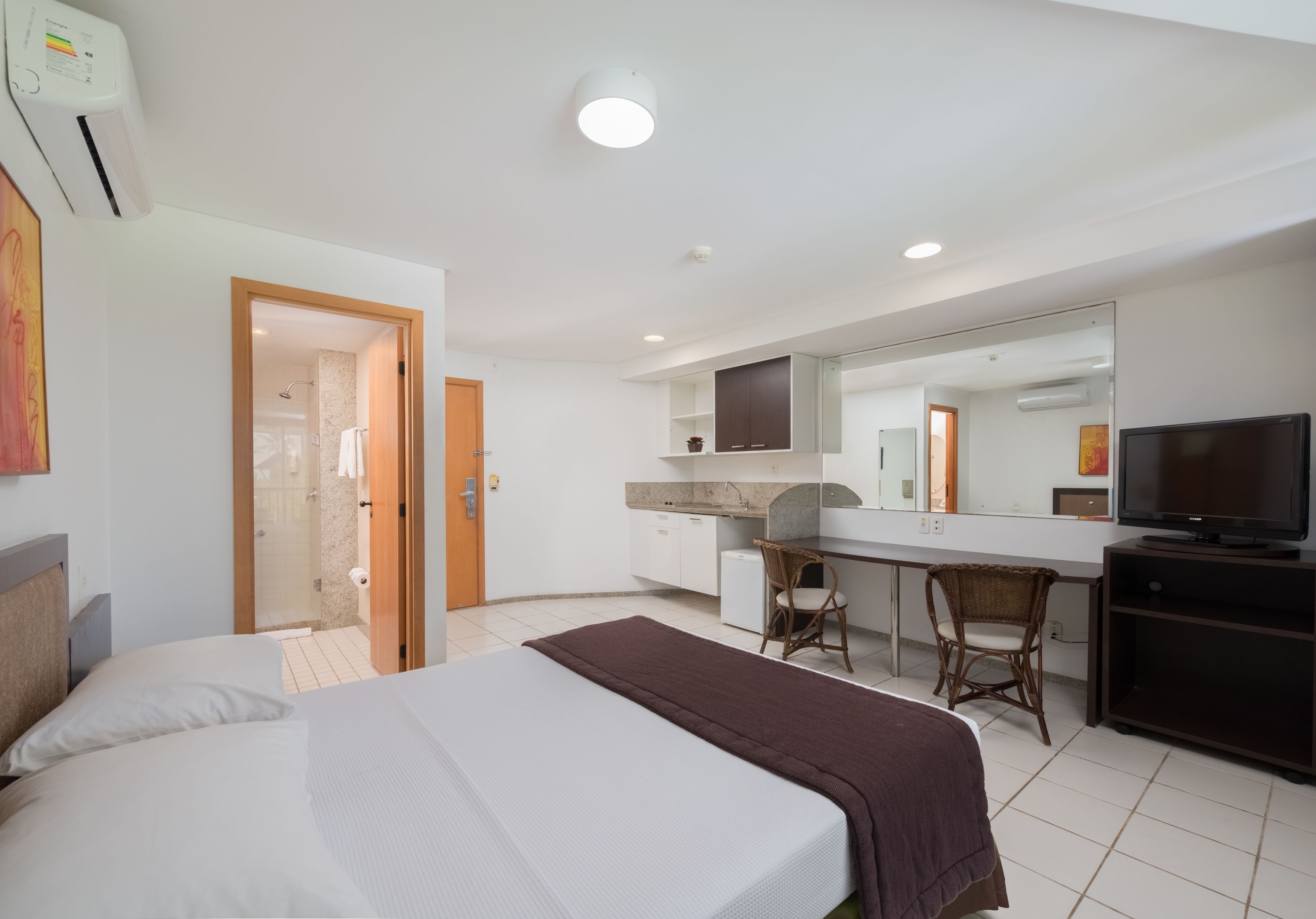 A hotel room with a bed, a desk, a chair, a television, and a bathroom with a shower.