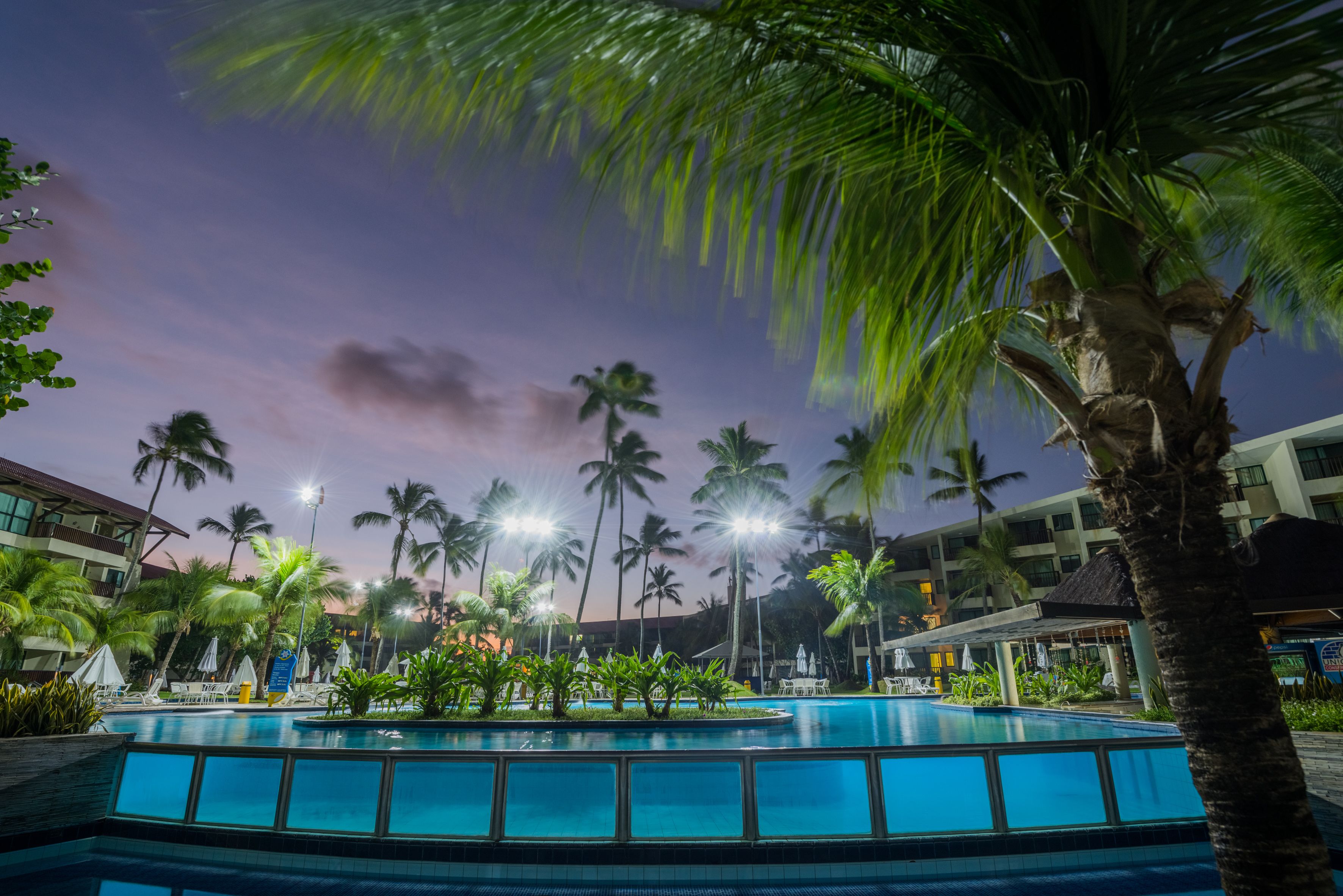 A swimming pool surrounded by palm trees and hotel buildings.