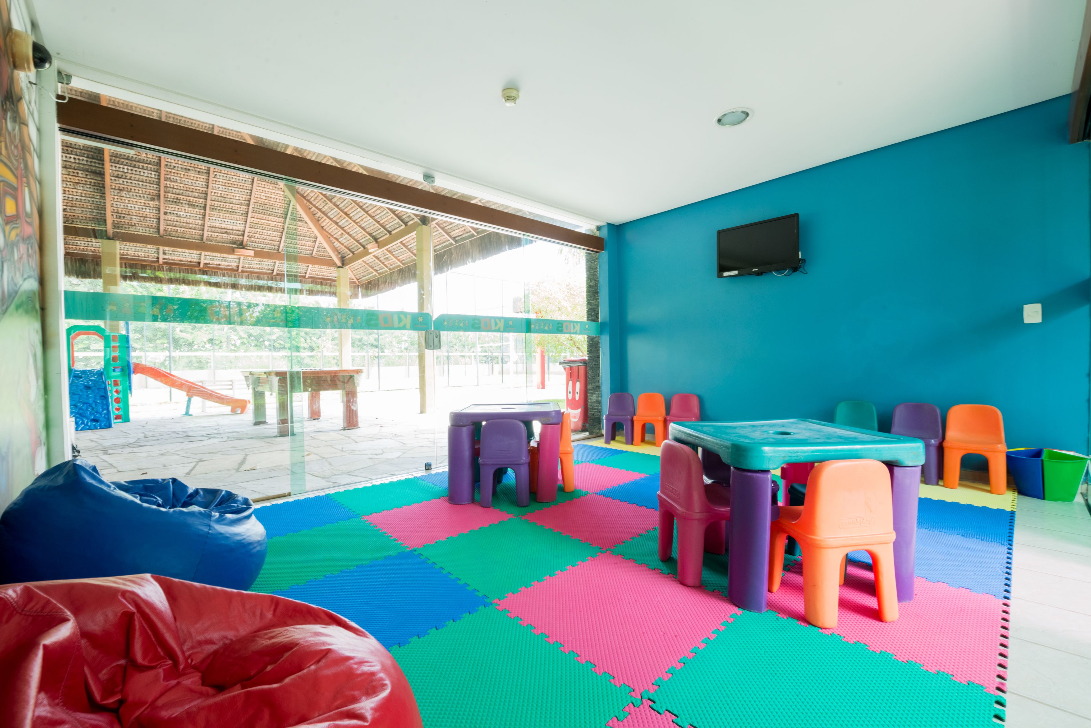Une pièce avec des tapis de jeu colorés, une table, des chaises et des fauteuils en forme de poire.