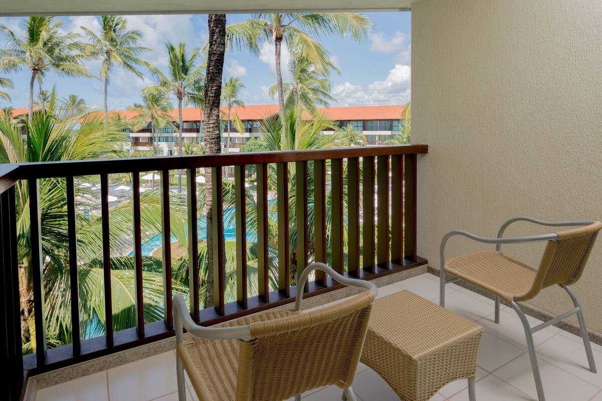 Ein Balkon mit Korbstühlen und Blick auf einen Pool und Palmen.