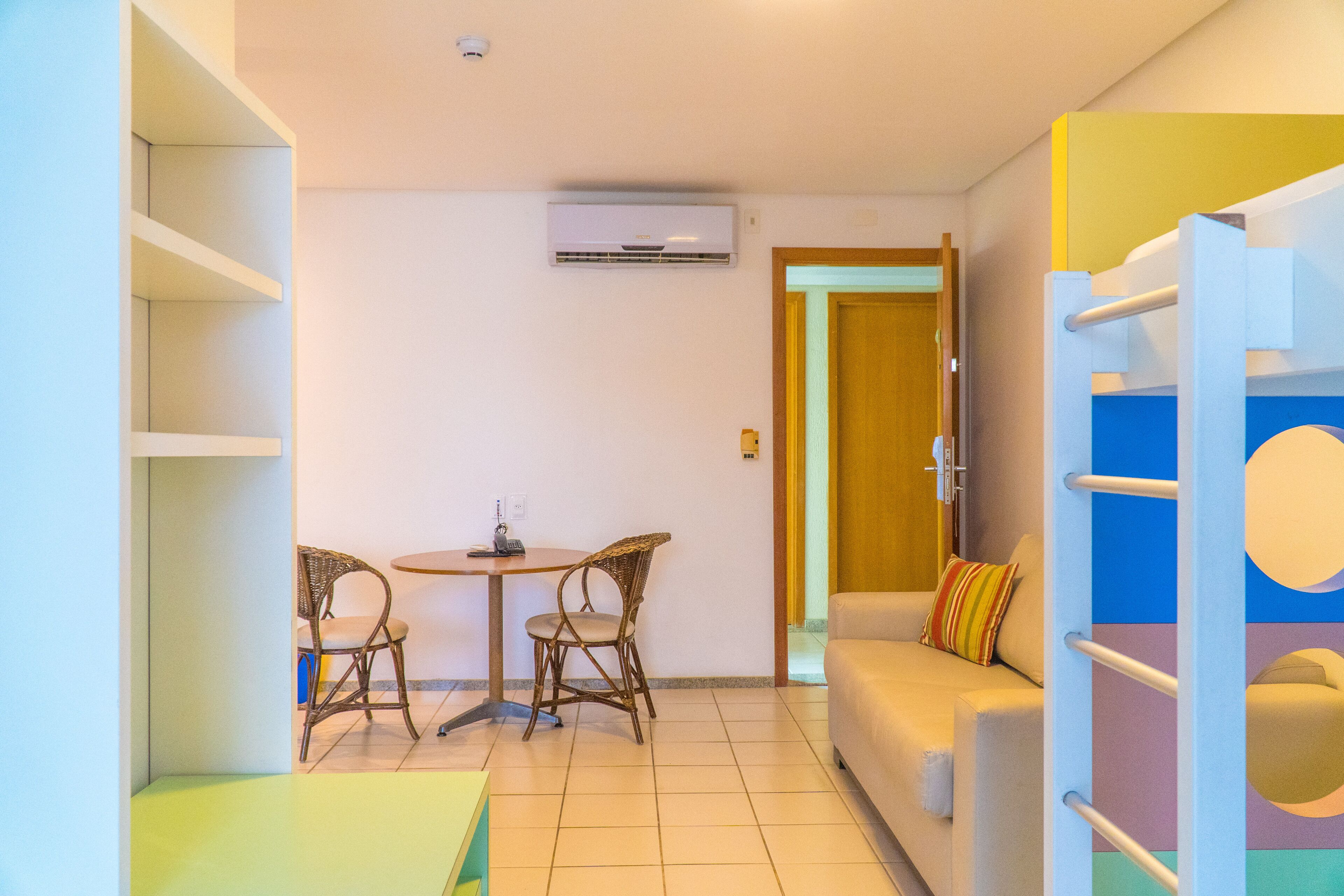 A compact room with a sofa, two wicker chairs, a small table with a phone, and an air conditioning unit on the wall.