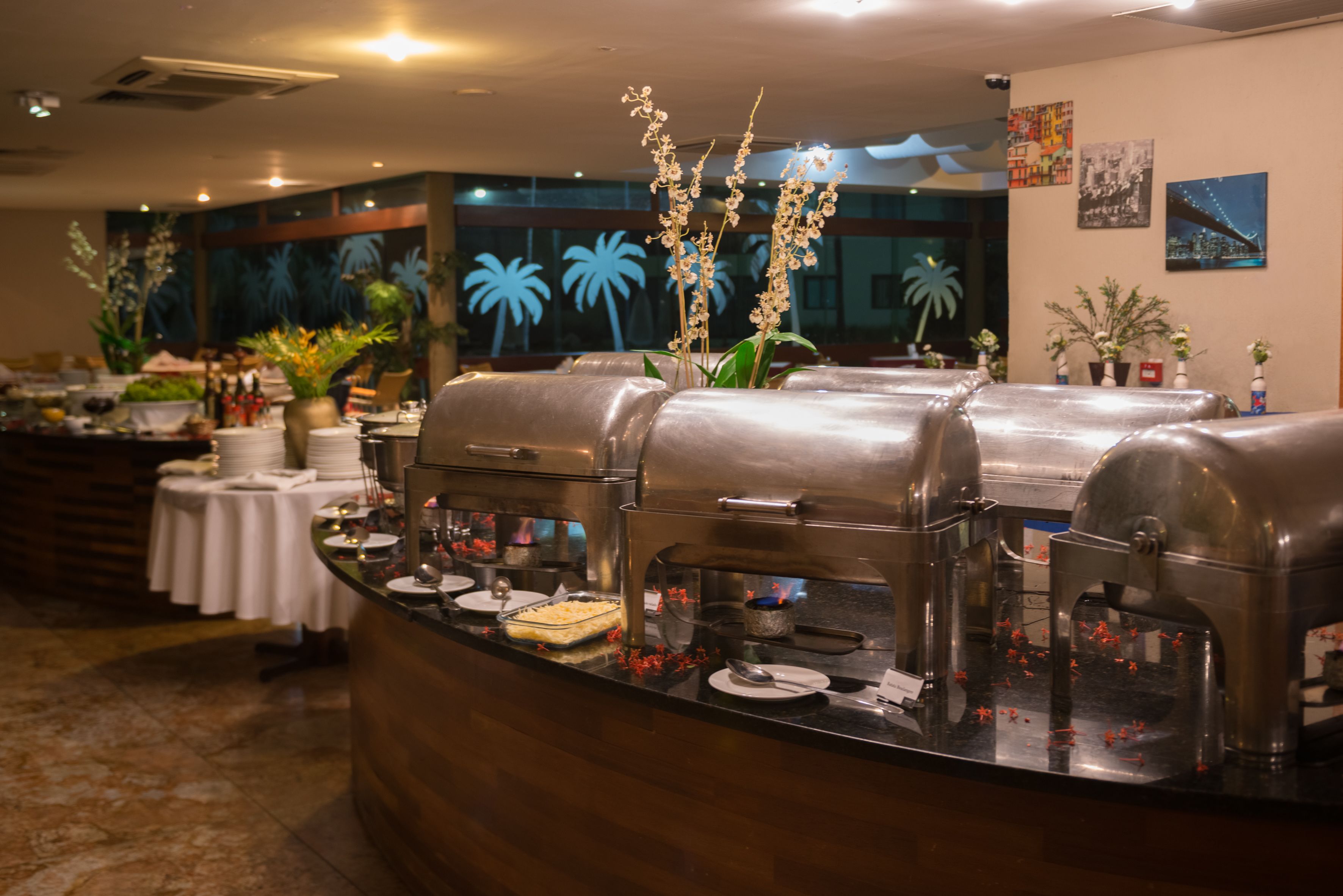 A buffet setup with multiple food stations, a counter with plates and utensils, and decorative plants.