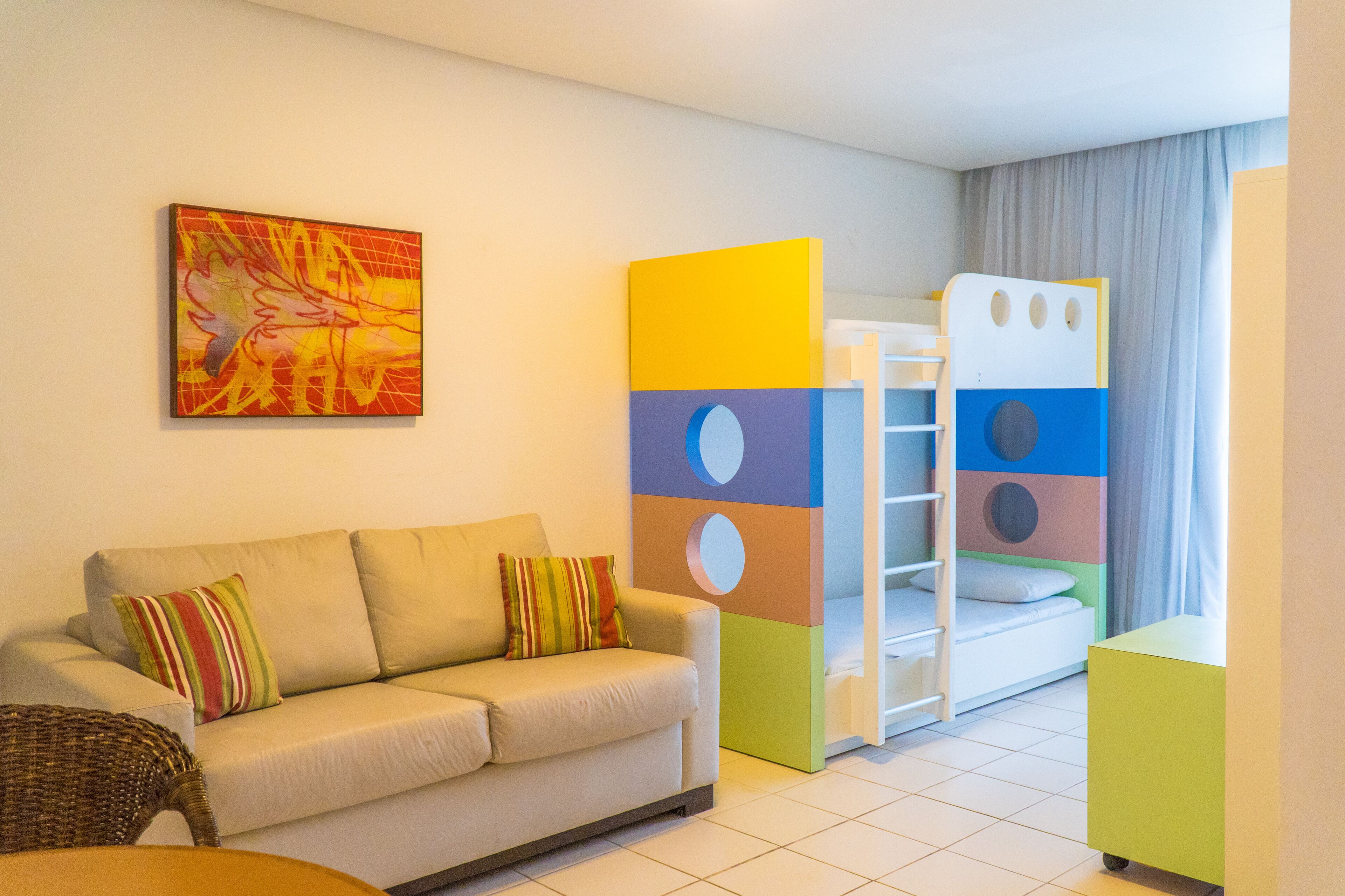 Una habitación de hotel moderna con sofá, una estructura de juegos colorida y un cuadro en la pared.