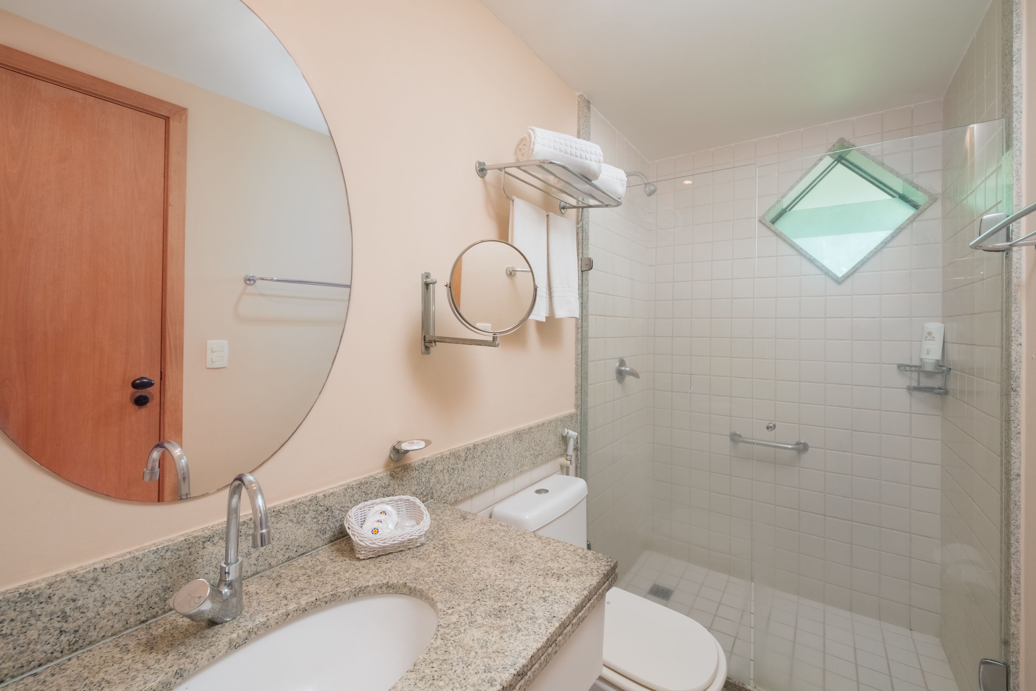 A bathroom with a sink, mirror, towel rack, and a shower area.