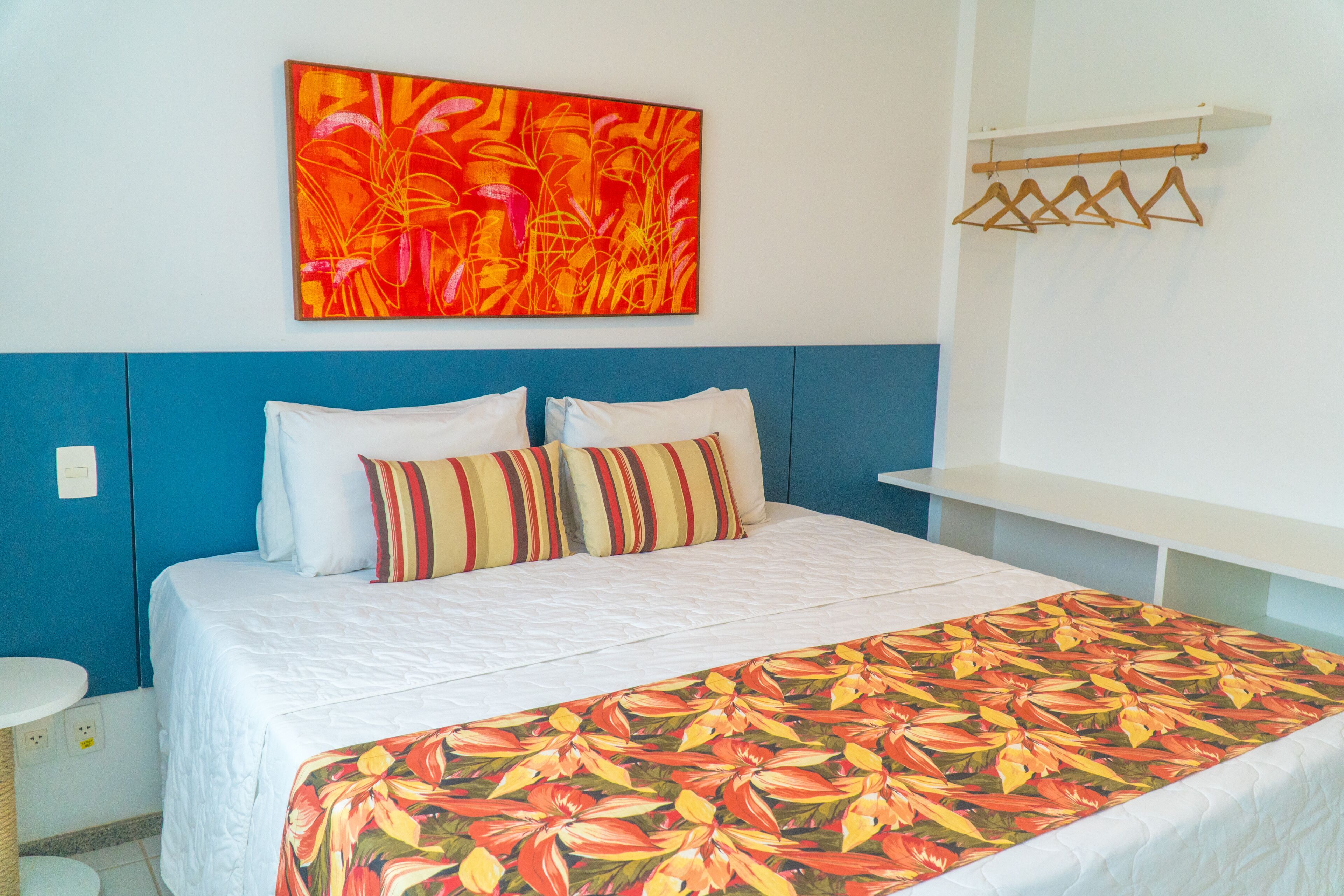 A bed with a floral bedspread, a blue headboard, and a colorful abstract painting above it.