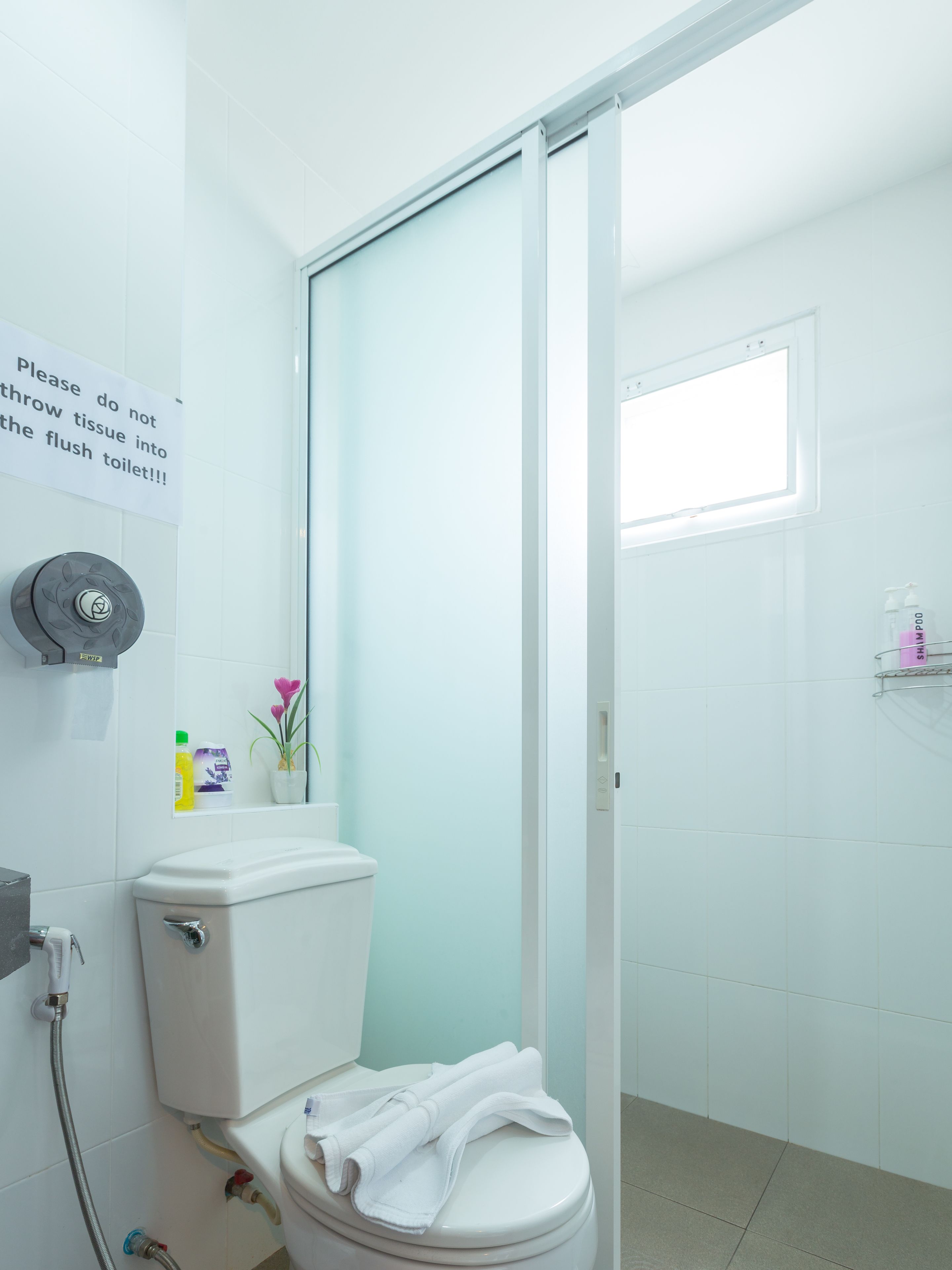 A bathroom with a toilet, a shower, and a sink. There is a sign on the wall instructing not to throw tissue into the flush toilet.