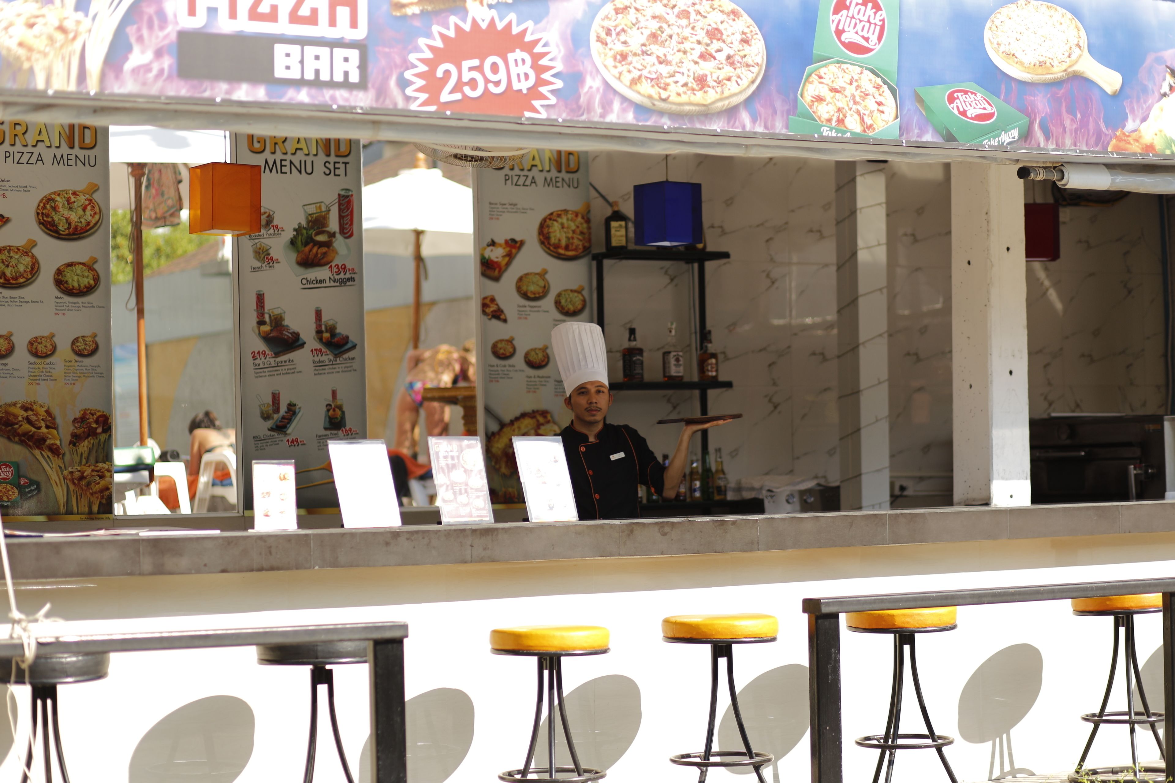 A pizza bar with a menu, a counter, and bar stools.