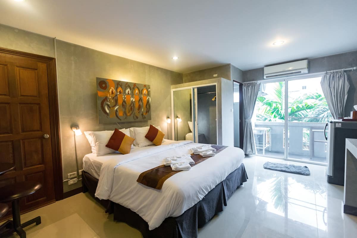 Ein Hotelzimmer mit einem großen Bett, einem Bild an der Wand, einer Tür und Blick ins Freie.