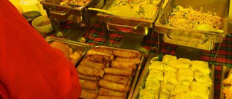 Una mesa de bufé con diversos alimentos, incluyendo rollitos fritos, un plato cremoso y un plato de fideos.