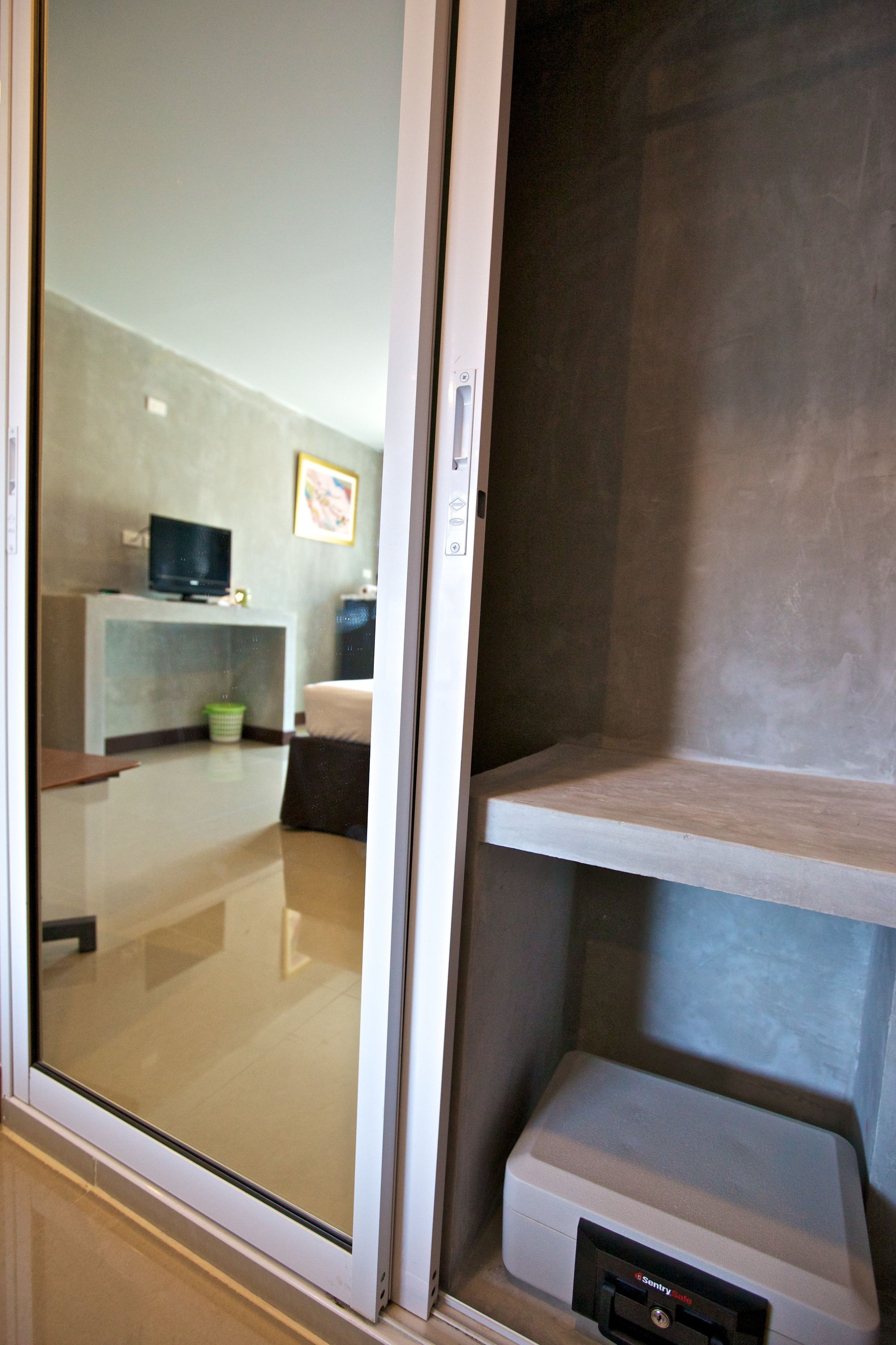 Habitación de hotel con puerta de vidrio, una cama, un televisor sobre un mueble bajo y un escritorio pequeño con una silla.