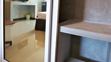 Habitación de hotel con puerta de vidrio, una cama, un televisor sobre un mueble bajo y un escritorio pequeño con una silla.