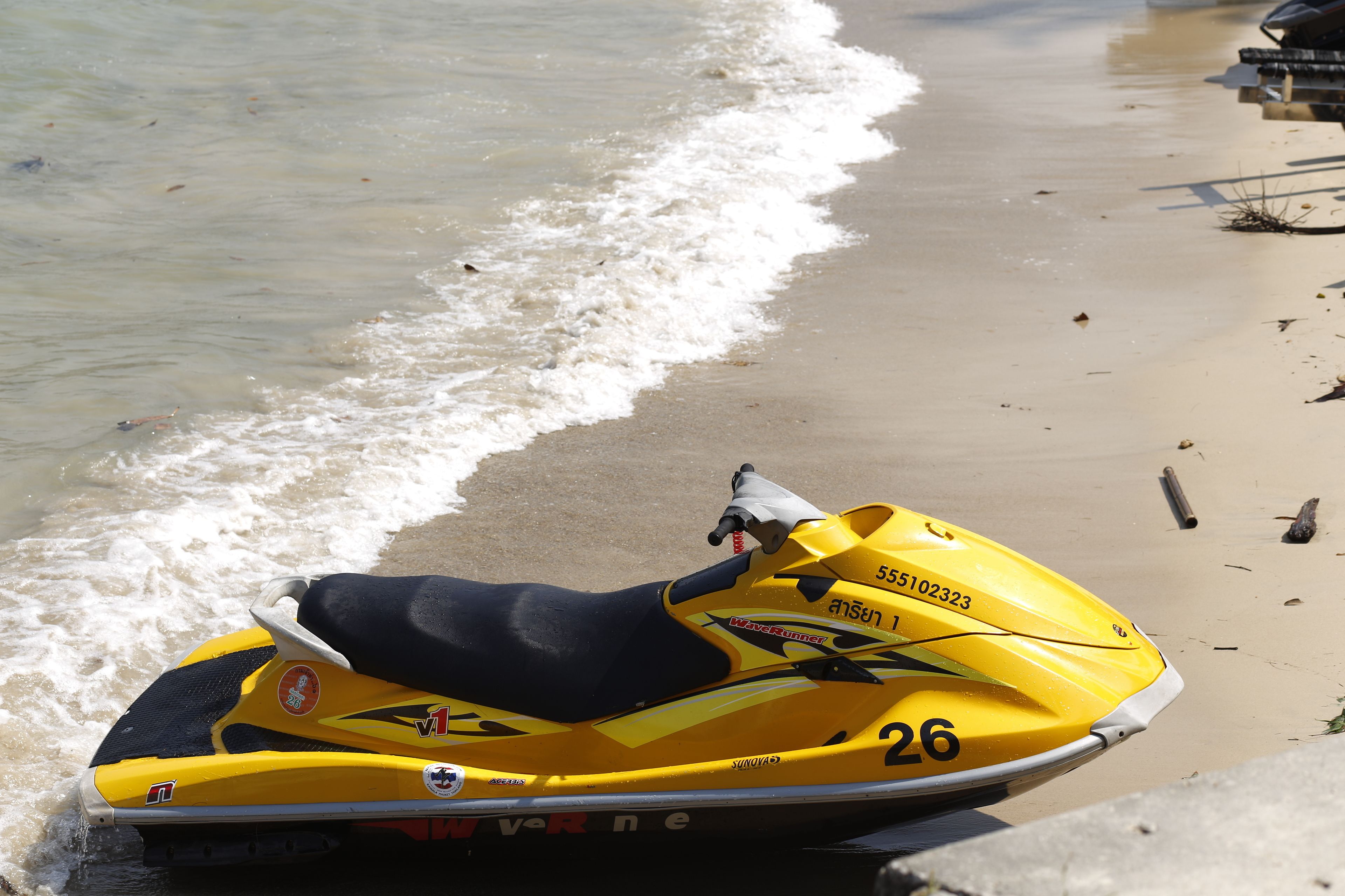 A yellow jet ski on a sandy beach near the water.