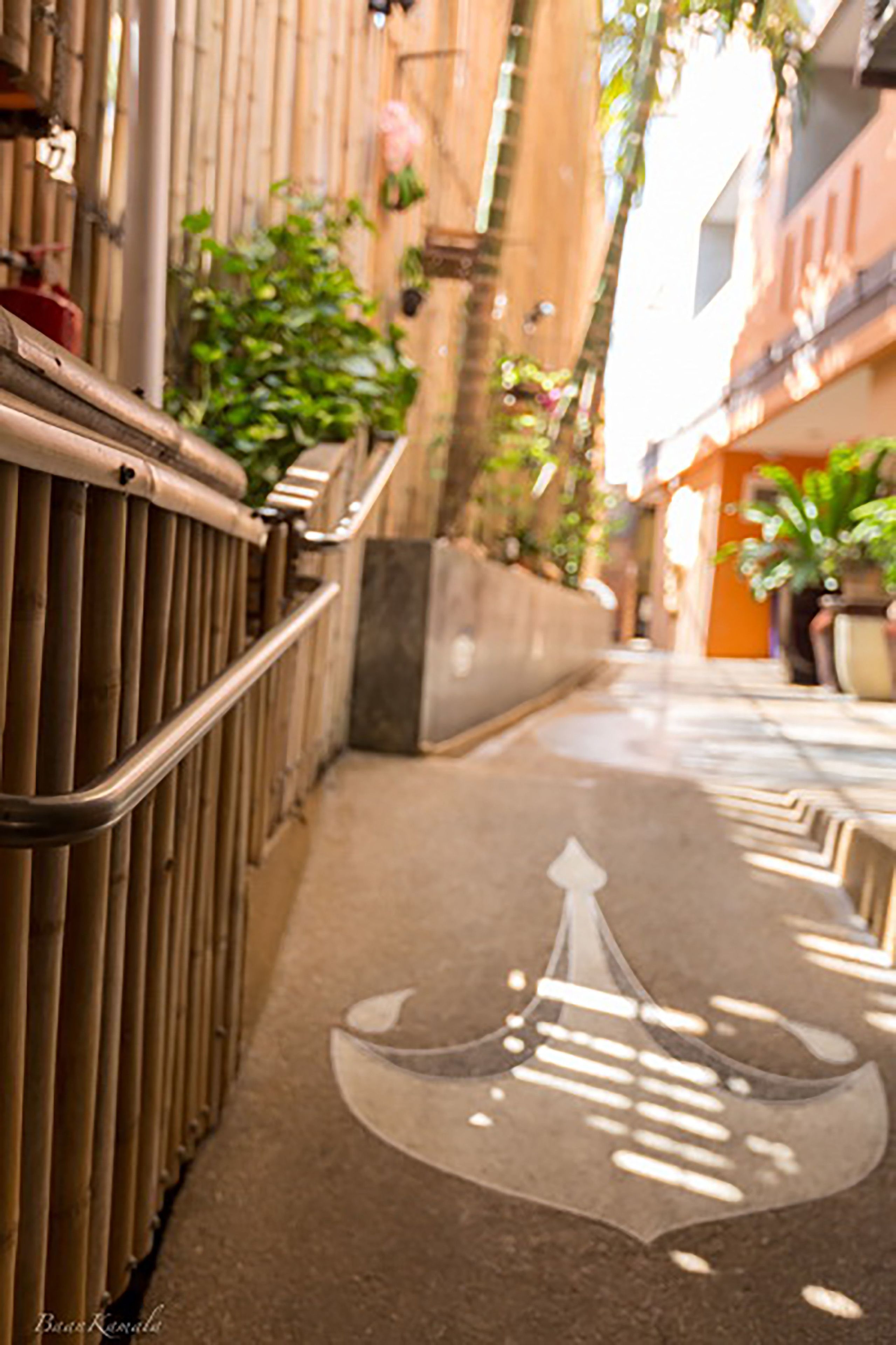 A narrow alleyway with a metal railing on one side and a concrete path with a bicycle symbol.